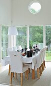 White, upholstered chairs around festively set dining table in front of glass walls