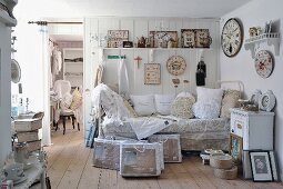 Daybed with lace cushions below collection of vintage clocks on white wooden wall and vintage-style ornaments on bracket shelf
