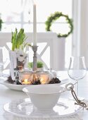 Place setting on dining table; bowl with handle decorated with cord, glass plate, wine glass and centrepiece on plate in background