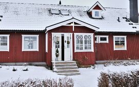 Falu-red, Scandinavian wooden house with snowy roof and decorated front door on projecting porch