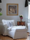 White chaise in front of antique, delicate side table below gilt-framed painting on wall