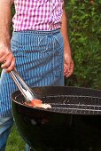 A man wearing an apron grilling salmon trout fillet in a garden