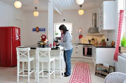 weiße, skandinavische Landhausküche mit rotem Retro-Kühlschrank; Frau beim Einschenken an der Frühstückstheke