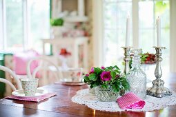 Bowl of flowers, crystal carafe and candlesticks on lace doily on dining table