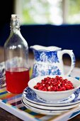 Bowl of fresh wild strawberries on stacked plates and blue and white jug next to vintage bottle in background