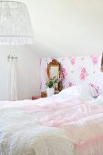 Double bed with pink lace bedspread against vintage-style floral wallpaper