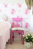 Pink lackierter Stuhl mit Schnitzereien und Sitzpolster, vor Blumentapete und Blumenstrauss im Schlafzimmer