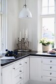 Silver candlesticks on L-shaped kitchen base units below retro pendant lamp