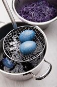 Eggs dyed using red cabbage on sieve spoon and pot of red cabbage