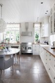 Essplatz mit Polsterstuhl in weisser Landhausküche, mit grossformatigen Steinbodenfliesen