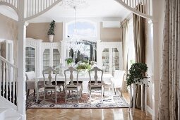 Elegant dining room with antique chairs around long table; foot of staircase and white, wooden column in foreground