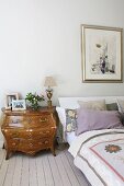 Rococo-style chest of drawers next to bed on pale wooden floor in rustic bedroom