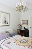 Patterned blanket on double bed with stack of scatter cushions against headboard; antique desk in background