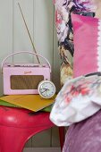 Rosa Retro Radio und Wecker auf pinkfarbenem Vintage Hocker und grossblumiger Bettbezug