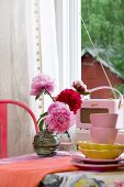 Vintage accessories in shades of pink and red with stacked crockery, retro radio and vase of peonies