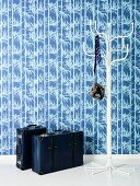 Koffer und weisser, filigraner Garderobenständer vor Wand mit weiss-blauer Tapete