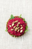 A slice of wholemeal bread topped with beetroot paste and pumpkin seeds