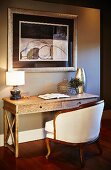 Antique armchair with white upholstery and curved legs at rustic writing desk below framed picture on wall painted light grey