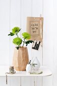 Three chrysanthemum 'Anastasia' flowers in mango-wood vase on white metal table; vintage items decorating wall