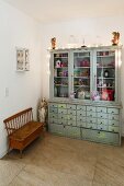 Apothecaries' cabinet with glass-fronted top next to Madonna statue and wooden bench