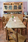 Solid wood dining table and chairs in front of dresser with fairy lights against pink-painted wall