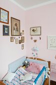 Kinderbett mit Stofftieren in Zimmerecke, an rosa getönten Wänden gerahmte Bilder
