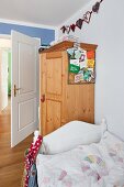 Bett mit weißem Holzgestell vor Bauernschrank im Kinderzimmer