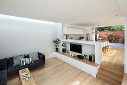 Open-plan, minimalist interior with sofa and dining area on raised platform separated by half-height wall