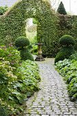 Cobbled path leading through topiary bushes to archway in hedge