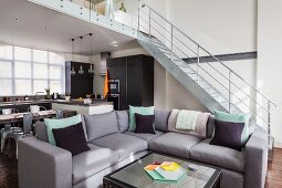 Grey sofa and coffee table in open-plan interior; fitted kitchen below gallery in background and metal staircase