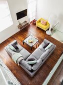 View down onto grey corner sofa and coffee table on dark parquet floor; yellow designer armchair and standard lamp in corner