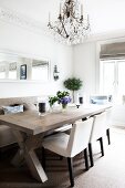 Comfortable dining area with chandelier above solid wood table and simple upholstered furnishings in kitchen-dining room