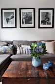 Retro black and white photos above sofa with collection of scatter cushions; vase of flowers and tealight holders in shades of blue on trunk table