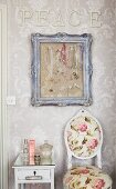 Schriftzug PEACE, Bilderrahmen mit aufgehängten Schmuckketten und blumiger Antikstuhl in romantischem Badezimmer