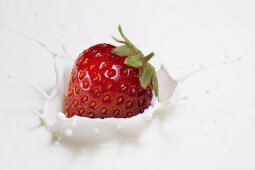 A fresh strawberry falling into milk