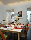 Dining table set with striped beakers and vase of flowers below pendant lamp in dining room