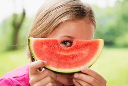A girl looking through a hole in a watermelon slice