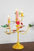 Lit candles in yellow-painted, romantic candlestick decorated with bird and flower ornaments