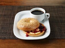 A sesame seed bagel with butter and jam served with coffee