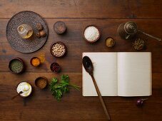 Various spices, chickpeas, rice, parsley and a blank cook book with a wooden spoon