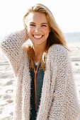 Junge, blonde Frau in beigefarbener Strickjacke am Meer