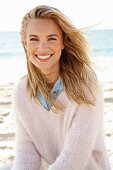 A young blonde woman by the sea wearing a denim shirt and a white woollen jumper