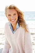 A young blonde woman by the sea wearing a denim shirt and a white woollen jumper