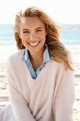 A young blonde woman by the sea wearing a denim shirt and a white woollen jumper