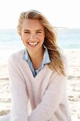 A young blonde woman by the sea wearing a denim shirt and a white woollen jumper