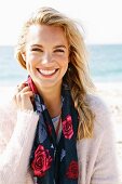 A young blonde woman by the sea wearing a light jumper and a scarf