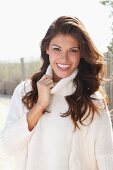 A young brunette woman outside wearing a white knitted roll-neck jumper