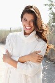 A young brunette woman outside wearing a white knitted roll-neck jumper