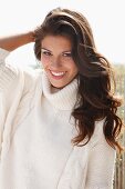 A young brunette woman outside wearing a white knitted roll-neck jumper