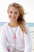 A young blonde woman by the sea wearing a light knitted jumper